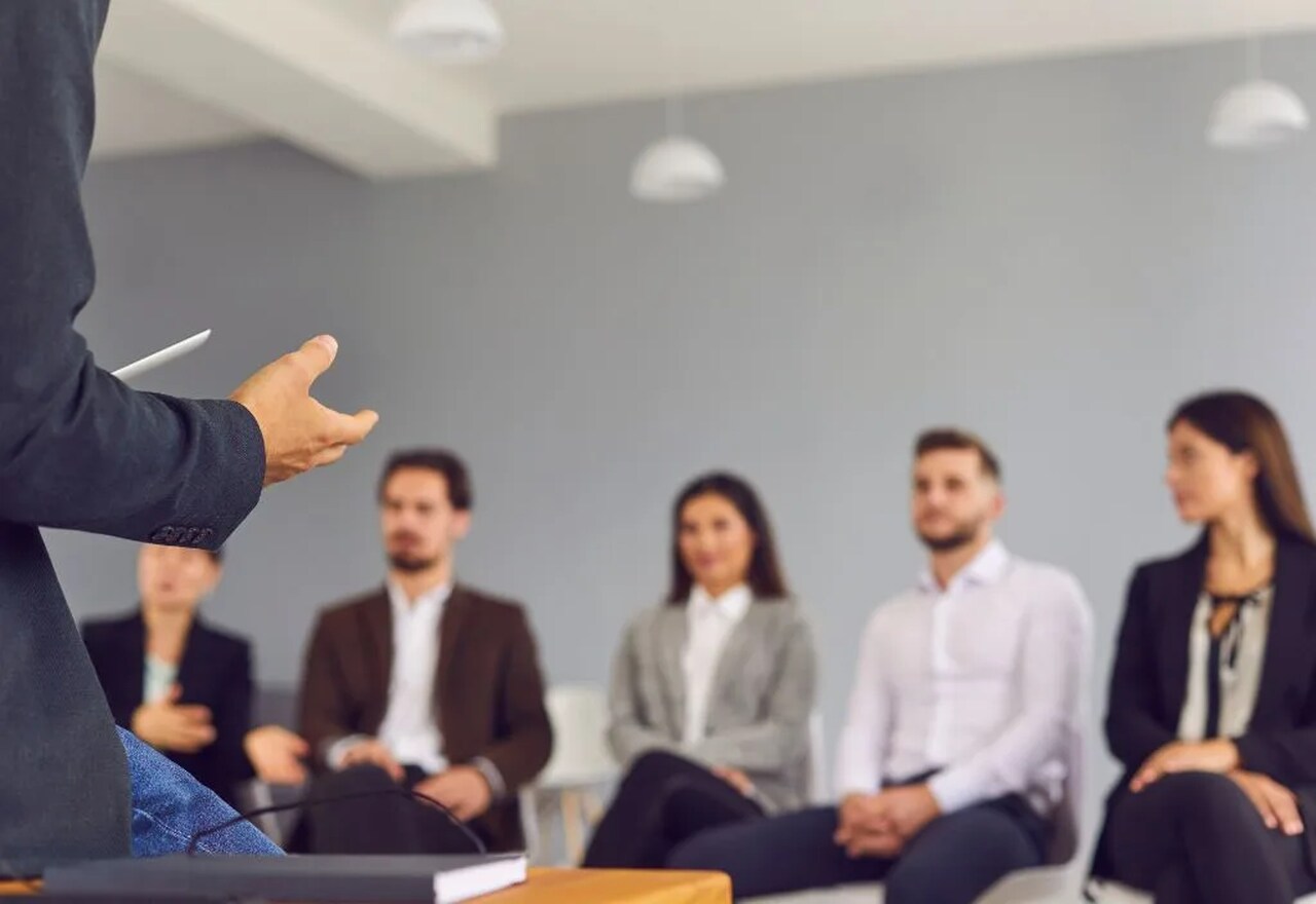 Homem dando treinamento sobre tipos de treinamento em RH para 5 pessoas sentadas